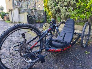 Accessible black and red TOP END Force-3 handcycle parked outdoors, promoting disabled-inclusive cycling with our Community Interest Company.